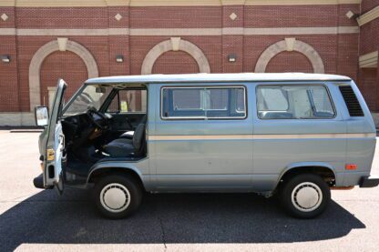 A gray volkswagen bus is parked in front of a brick building.