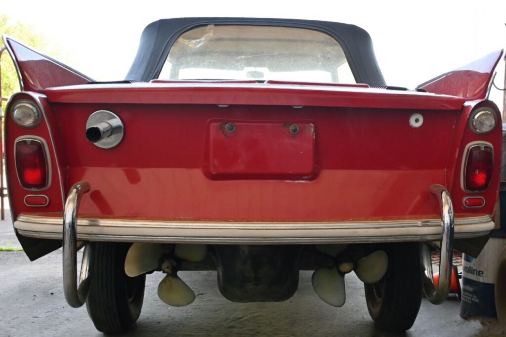 The rear end of a red car is parked in a garage.